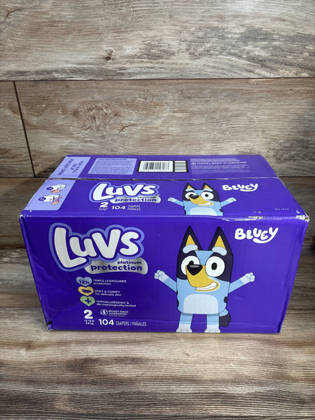 Front view of Luvs Platinum Protection Size 2 diaper box (104 count) showing Bluey character and branding on wooden tabletop