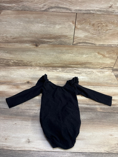 Front view of black long sleeve bubble romper showcasing flutter shoulder details with a wood-look floor background