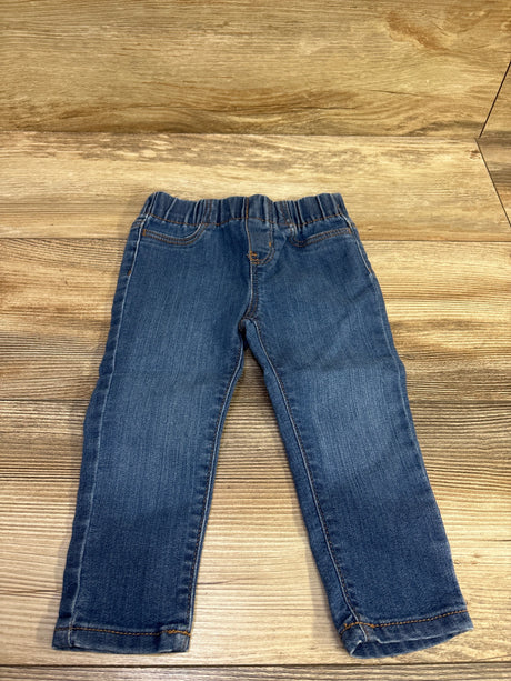 Front view of OshKosh blue denim jeggings in size 18 months showcasing elastic waistband and stitched pockets on a wood background
