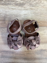 Top-down view of mauve baby sandals showcasing satin bows, ankle Velcro straps and cushioned insoles on light wood floor
