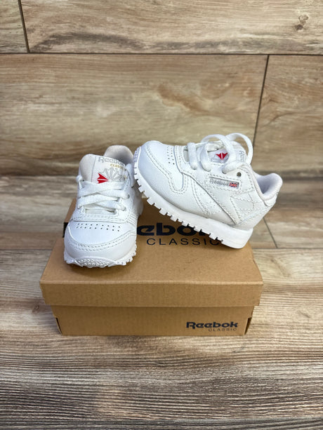 Angled front view of white Reebok Classic Leather infant sneakers showing leather upper, laces, logo on Reebok shoebox