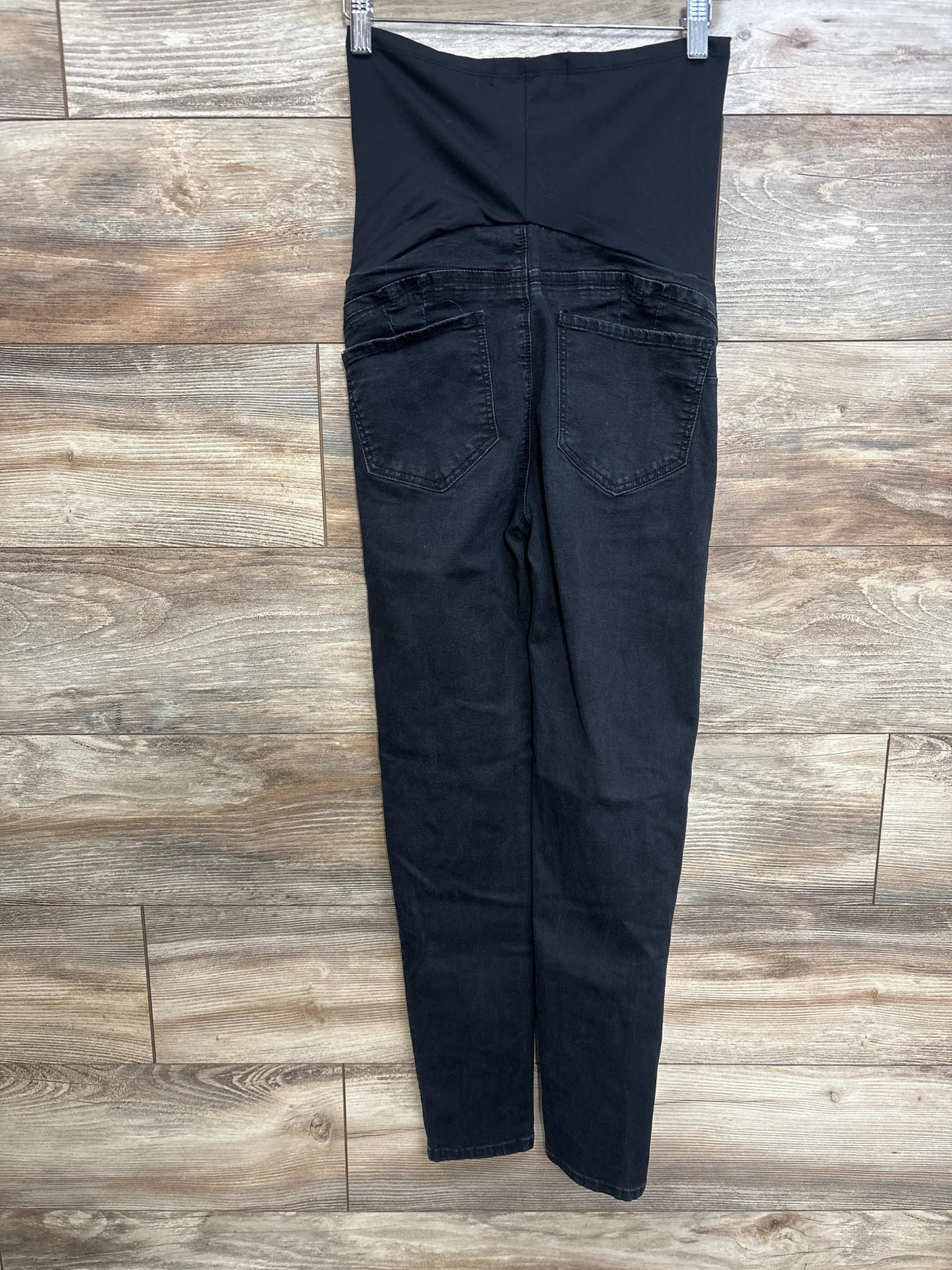 Back view of black maternity skinny jeans with tall stretch over-belly panel and back pockets on wood floor background