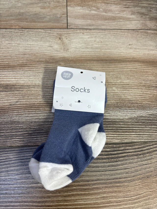 Front view of Fred and Flo baby socks showcasing blue knit with white toes and heels and tag reading Socks on wood floor