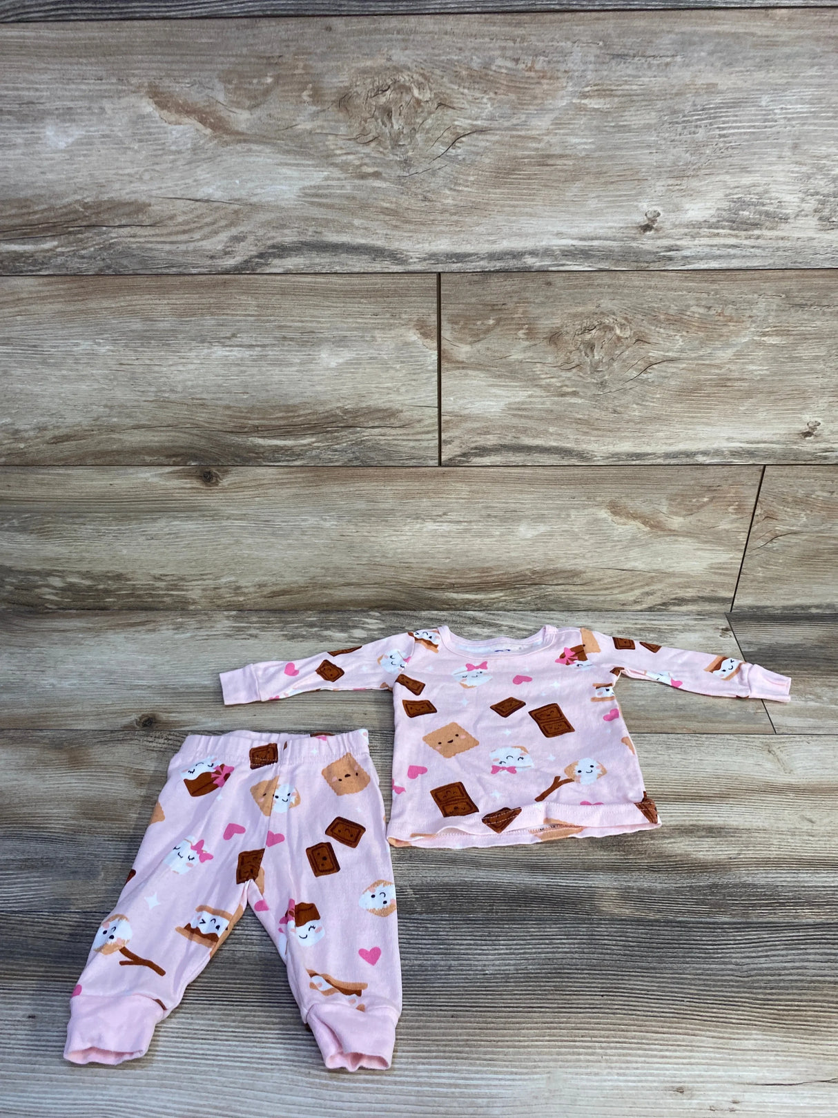 Flat lay of Children's Place pink 2-piece baby pajama set with s'mores print on top and pants on wood background