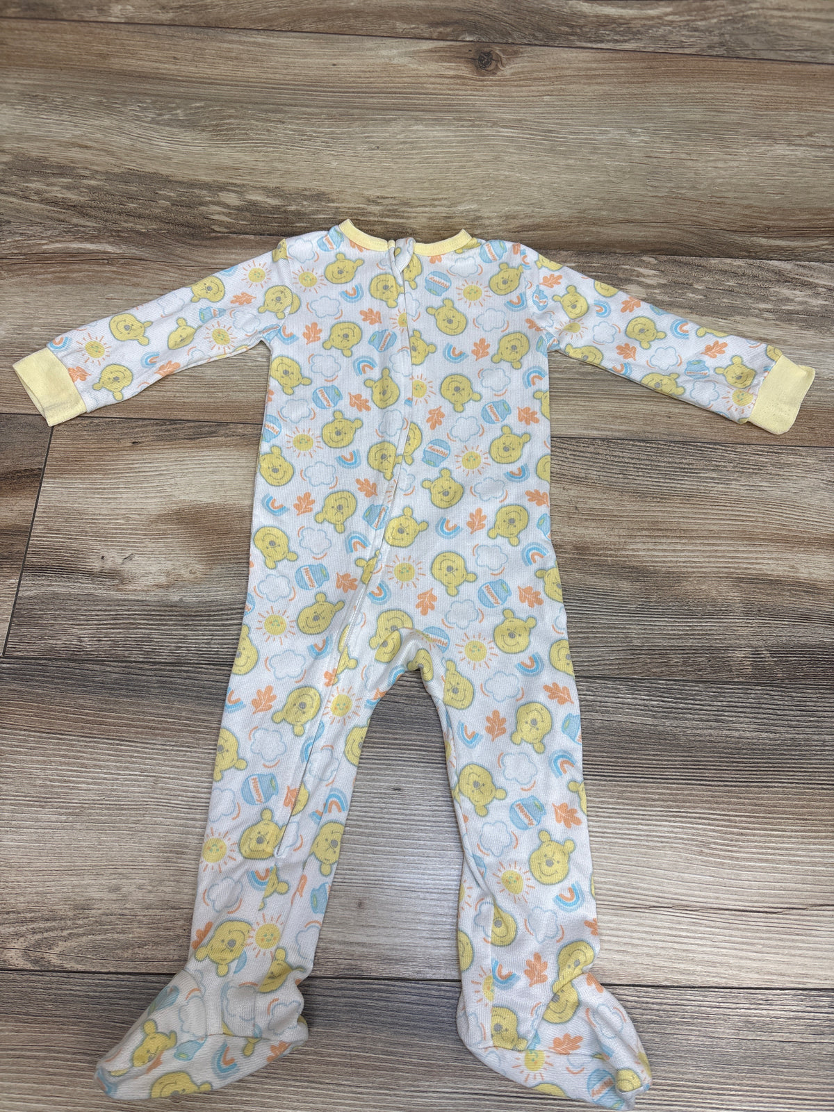 Front view of Disney Baby Winnie the Pooh sleeper showcasing footed legs and front zipper on a wood-grain surface