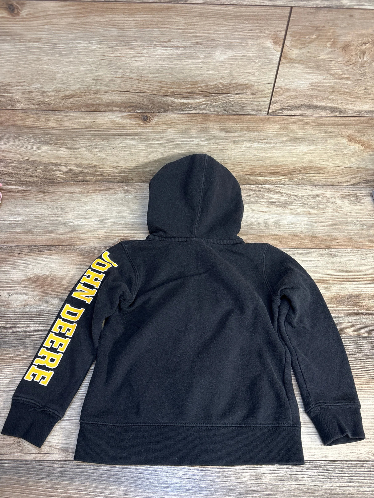 Black kids hoodie with yellow John Deere lettering on sleeve, displayed on wood floor