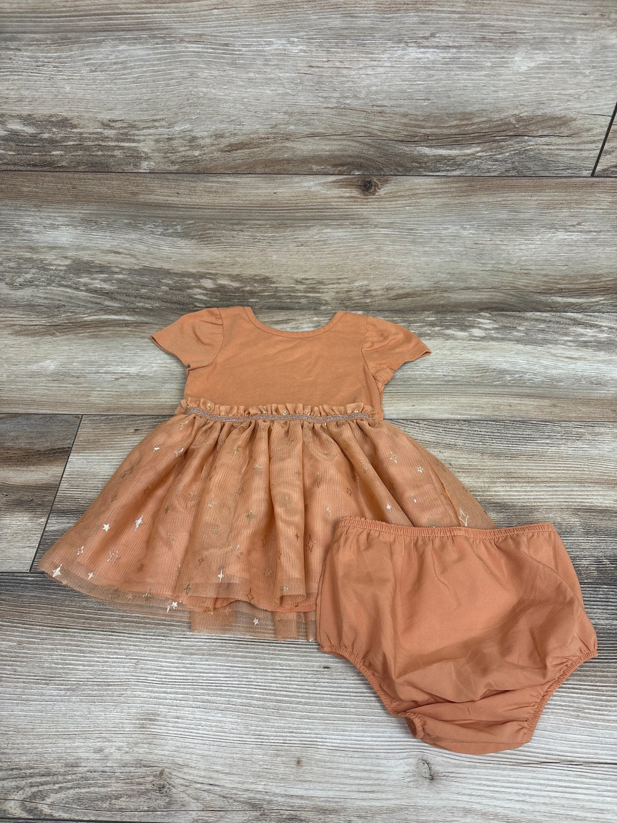 Top view of Cat & Jack two-piece orange dress set showcasing a star-print skirt and matching bloomers on wood background