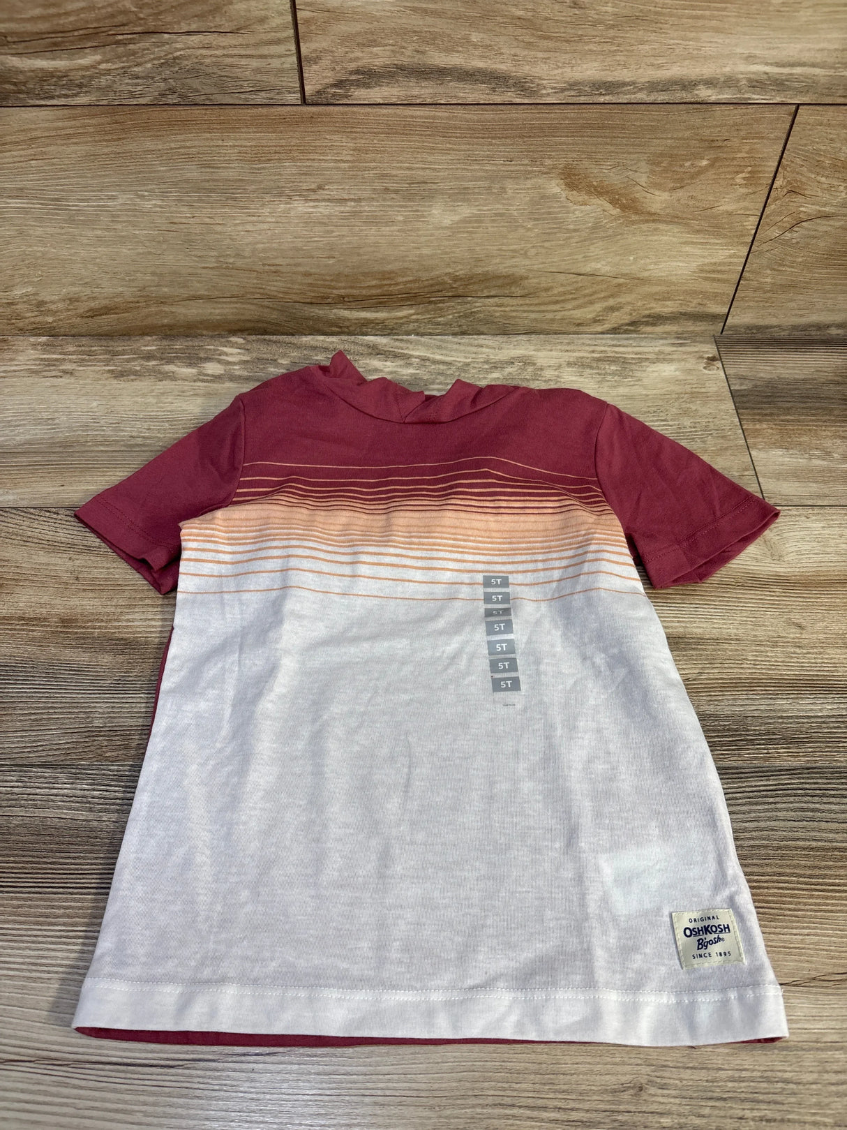 Top-down of maroon and white Oshkosh 5T hooded shirt with ombre stripes, brand patch and size stickers on wood floor