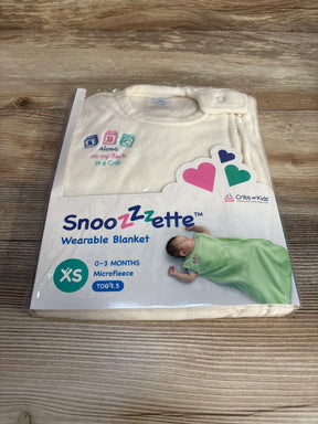 Cream Snoozzette wearable blanket for babies 0-3 months in microfleece, packaged on wood