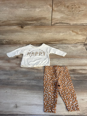 Baby outfit with white 'Happy' long sleeve shirt and brown floral leggings on wood floor