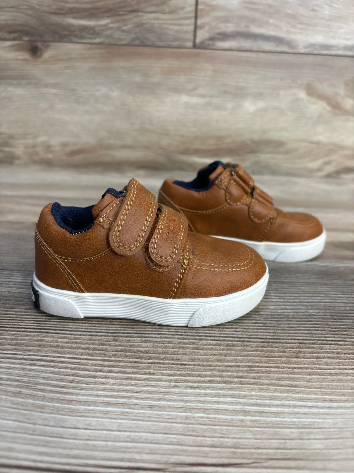 Brown toddler shoes with velcro straps, navy lining, white soles on wood floor
