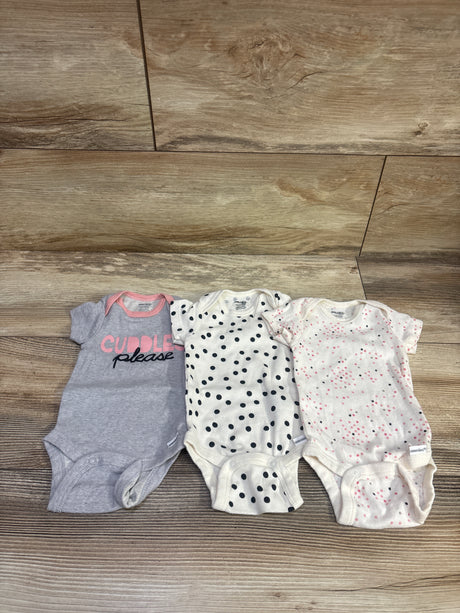 Top view of Gerber 3pk bodysuit set with gray CUDDLE please, black polka-dot, and pink-speckled bodysuits on wood floor
