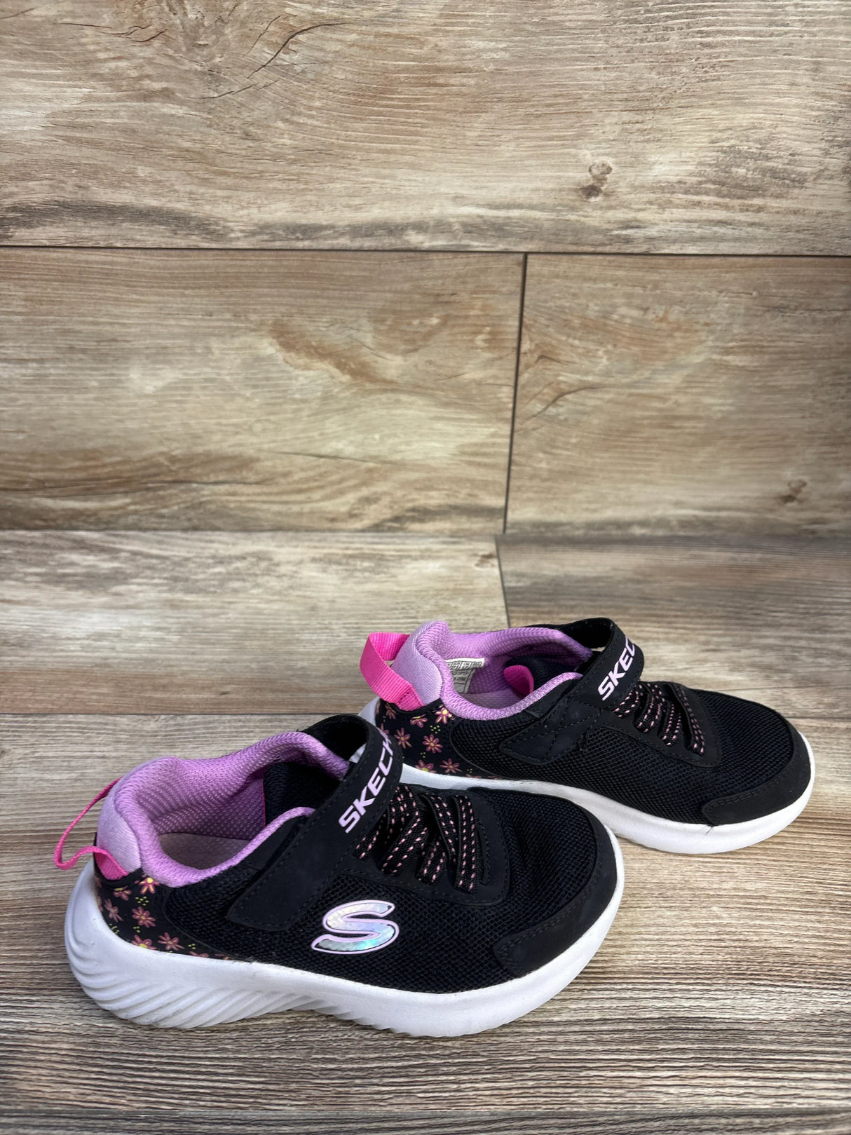 Side view of Skechers Ultra Flex black floral sneakers size 11C with pink lining, velcro strap and white sole on wood floor