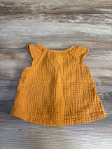Front flat lay of Cat and Jack gauze baby shirt, orange with ruffled cap sleeves on wood background