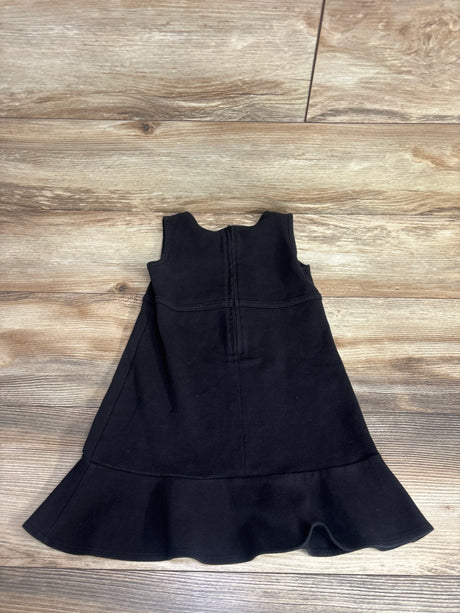Black sleeveless girls dress with ruffled hem, laid flat on wooden floor, kids clothing