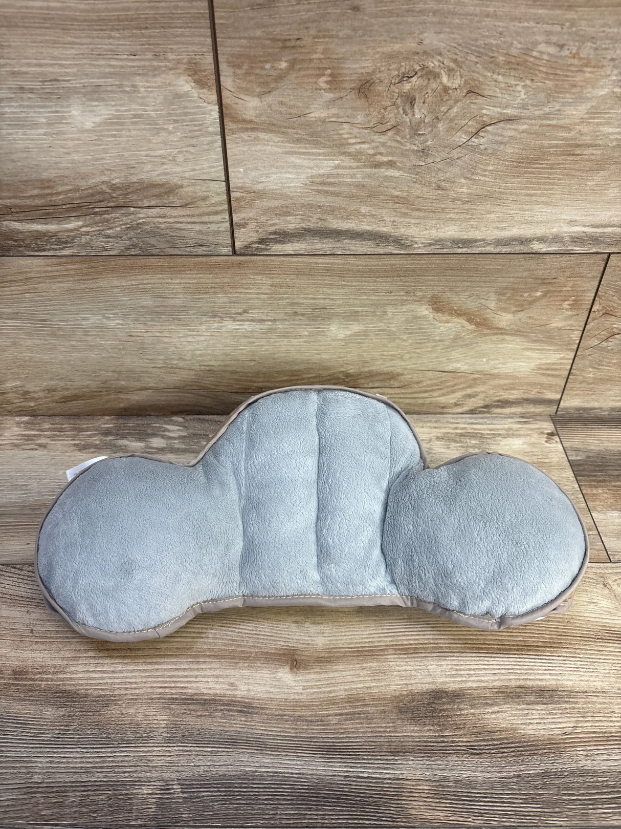 Top view of Taf Toys tummy time support pillow with grey plush cloud shape and raised side bolsters on wood background