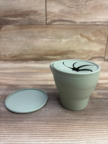 Front view of green silicone collapsible snack cup showcasing its petal opening and separate lid on a wood-grain background