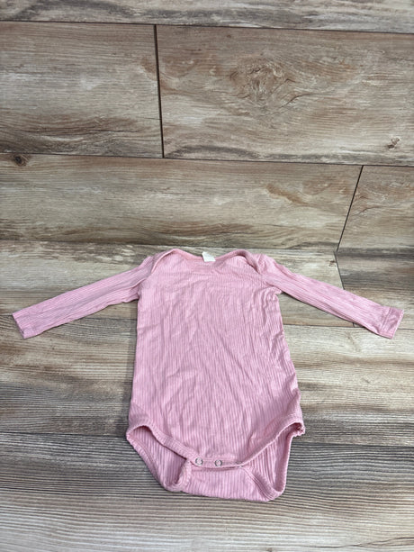 Front view of Kate Quinn pink ribbed modal long sleeve bodysuit for ages 6 to 12 months with snap closures on a wood-grain background