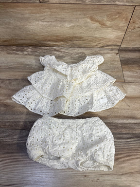 Top-down view of white tiered eyelet baby dress and matching bloomers showcasing ruffled tiers and elastic waist on wood floor