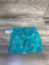 Flat lay of teal toddler swim trunks size 12M showcasing all-over pink flamingo print and elastic waistband on wood floor