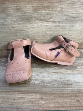 Pink leather toddler shoes with buckle straps and cutout floral details on wood background