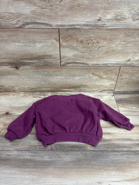 Top view of Grayson Mini Paris purple sweatshirt showcasing ribbed cuffs and waistband on a wood-grain background