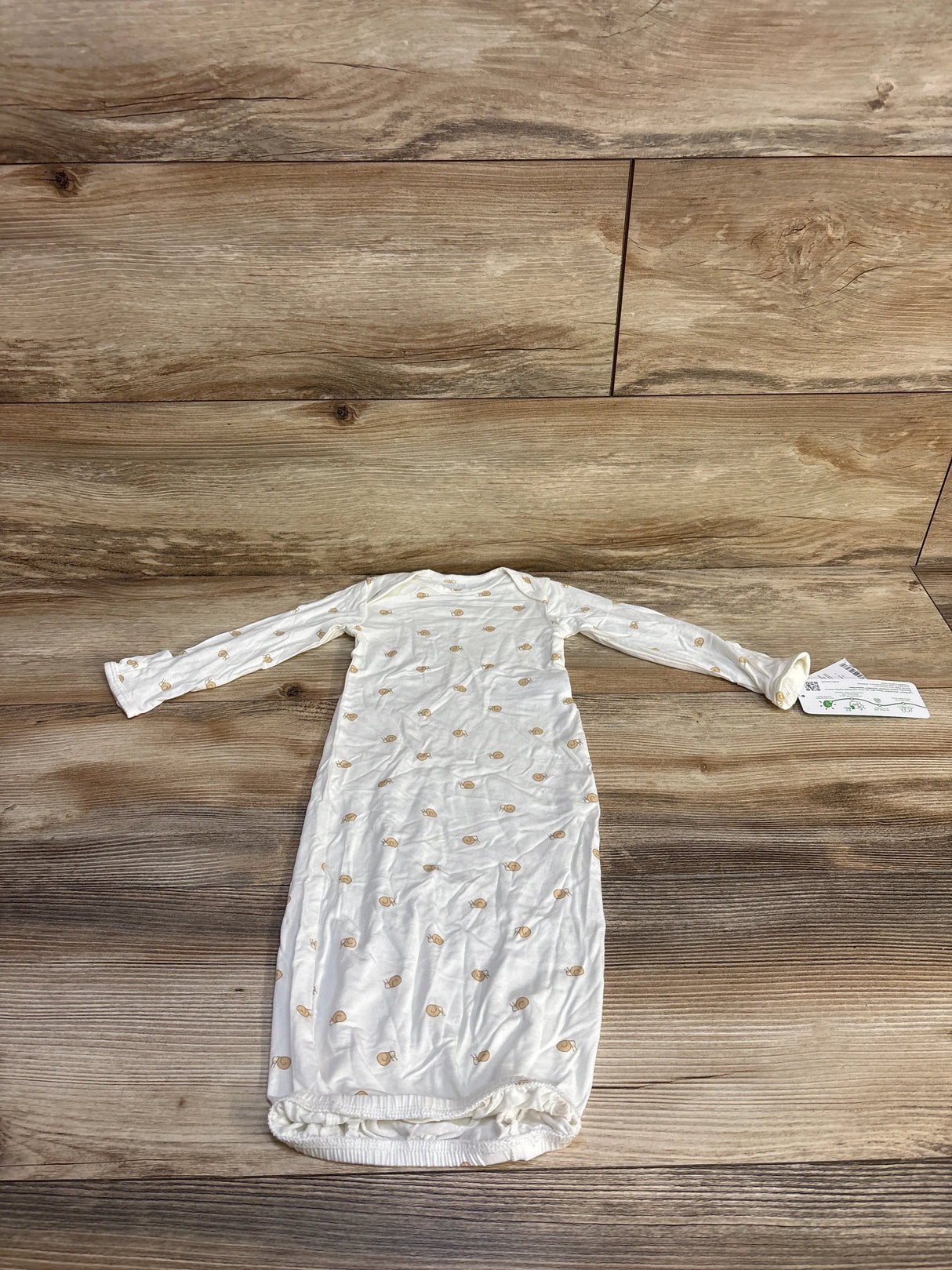 Flat-lay of Carter's white baby gown showing tan snail print, long sleeves, and elastic hem on wood background