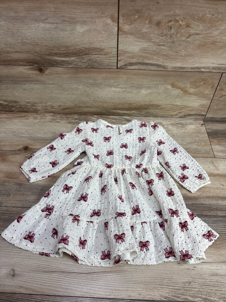 Top view of Nannette bow print long sleeve dress in ivory, showcasing gathered waist and tiered skirt on a wood floor