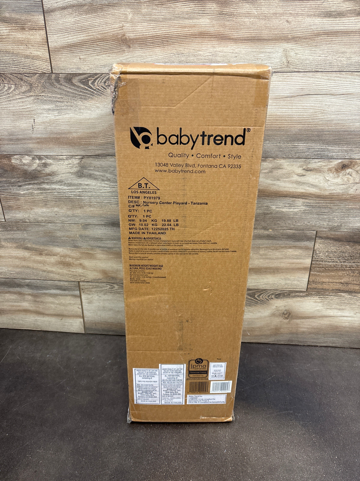 Front view of Baby Trend Nursery Center Playard Tanzania packaging showing product labeling on a wood floor