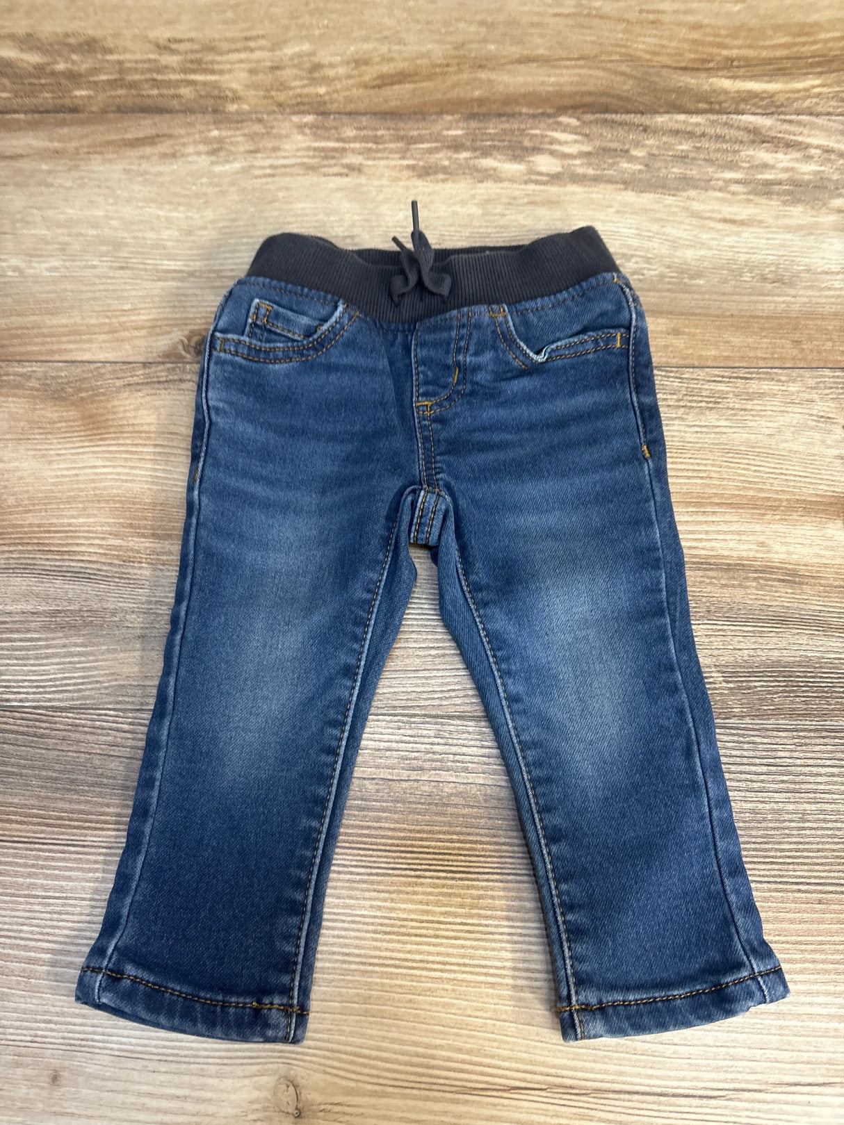 Flat lay of Wonder Nation toddler drawstring joggers, 12 months, showing elastic ribbed waistband and faded blue denim on wood