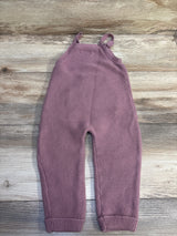 Top view of Little Planet knit overalls in mauve showcasing shoulder straps and ribbed cuffs with a wood grain background