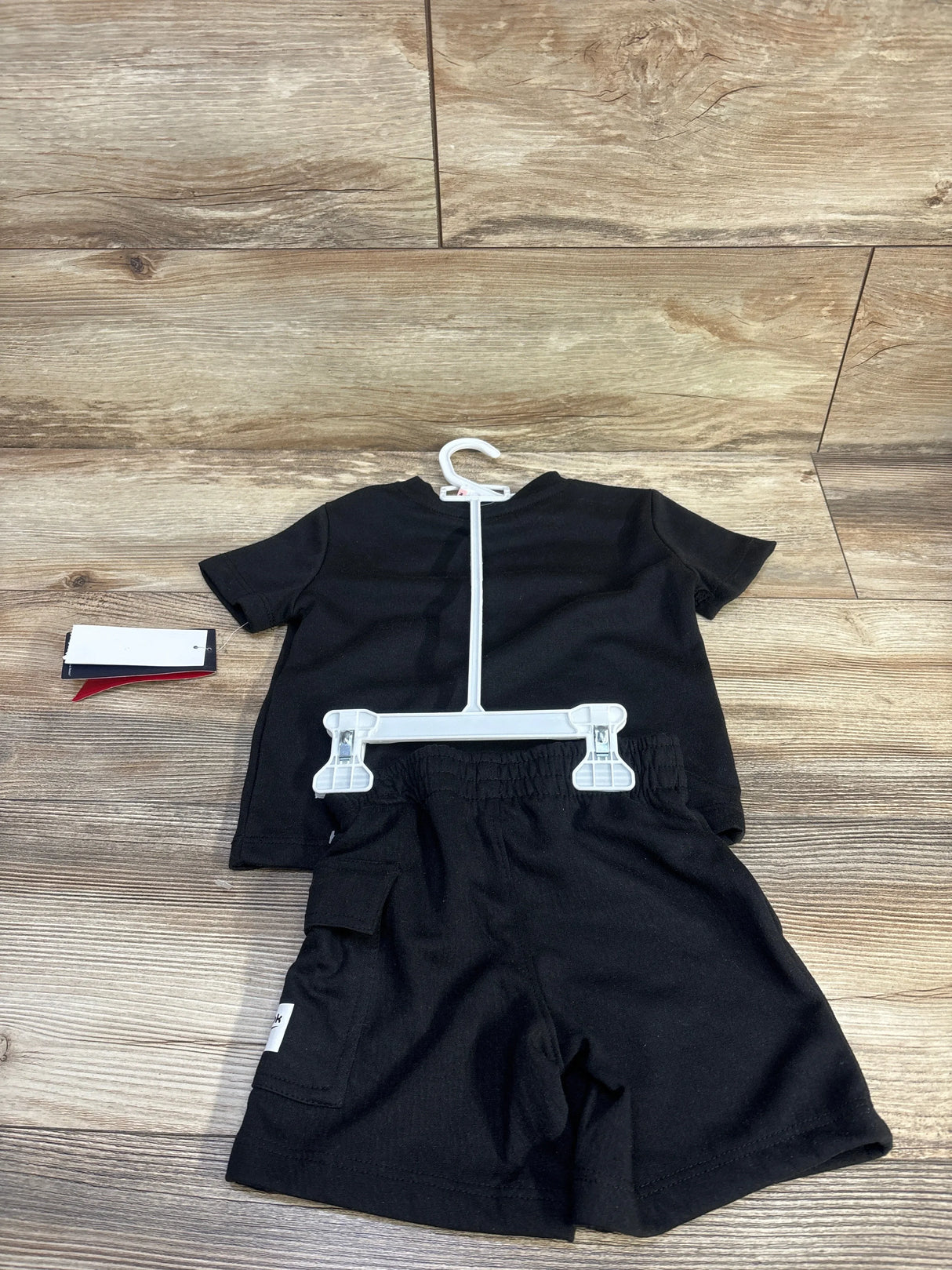 Flat lay of toddler Reebok black short-sleeve shirt and elastic-waist shorts showing side cargo pocket on wood background