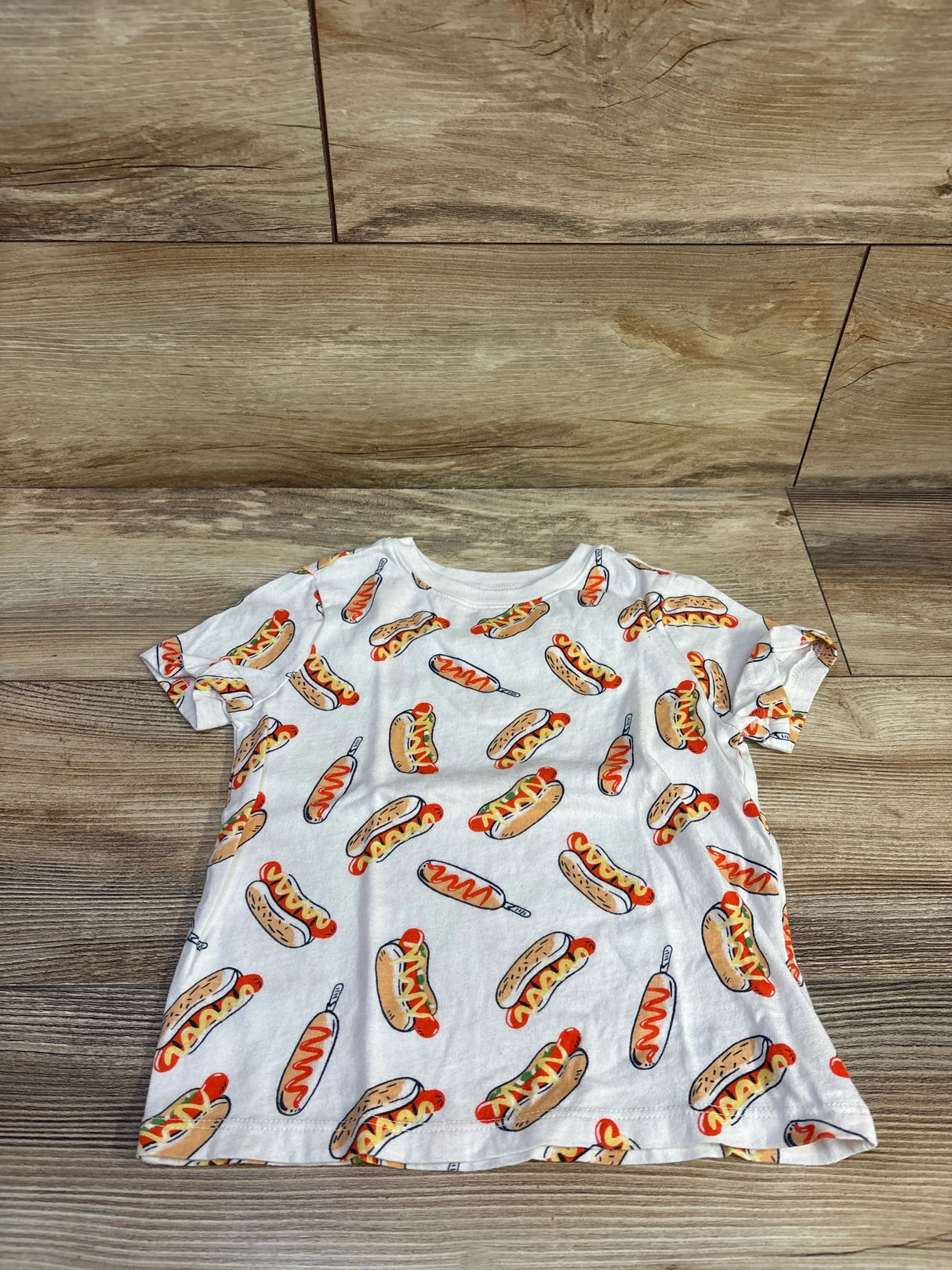 Flat lay of Old Navy toddler white t-shirt showing all-over hot dog and corn dog print on wood background