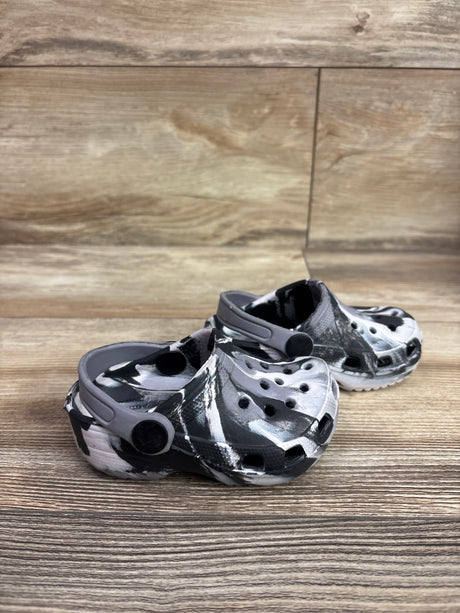 Three-quarter view of black and white marbled clogs, size 5C, showcasing perforated uppers and heel straps on a wood surface