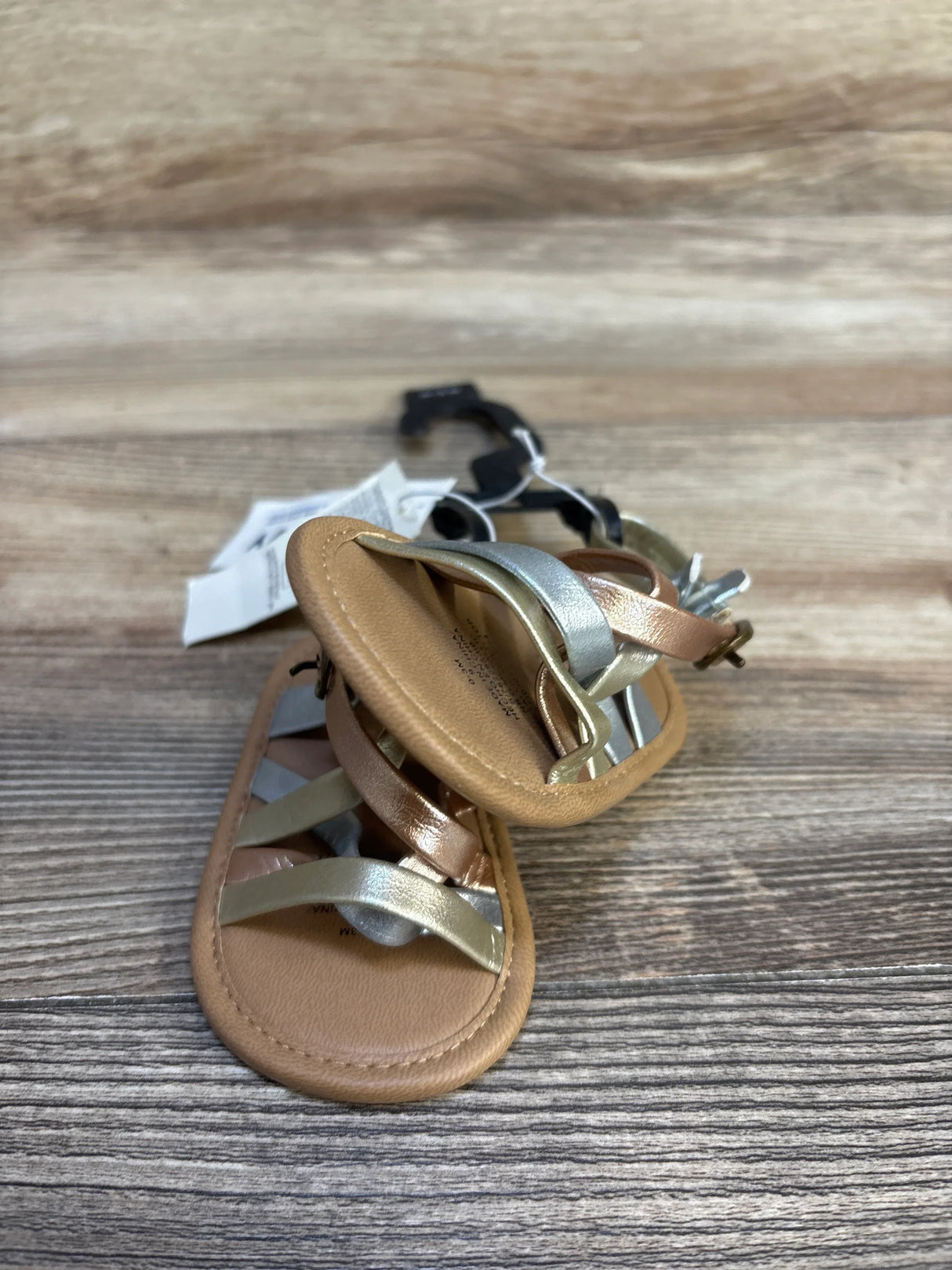 Metallic baby sandals with silver and rose gold straps on wood background