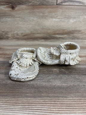 Pair of white snakeskin-patterned baby moccasins with fringe on wooden floor