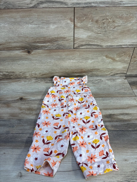 Flat lay of pink floral jumpsuit, 6-12m, showing ruffle shoulder straps and all-over flower print on wood background