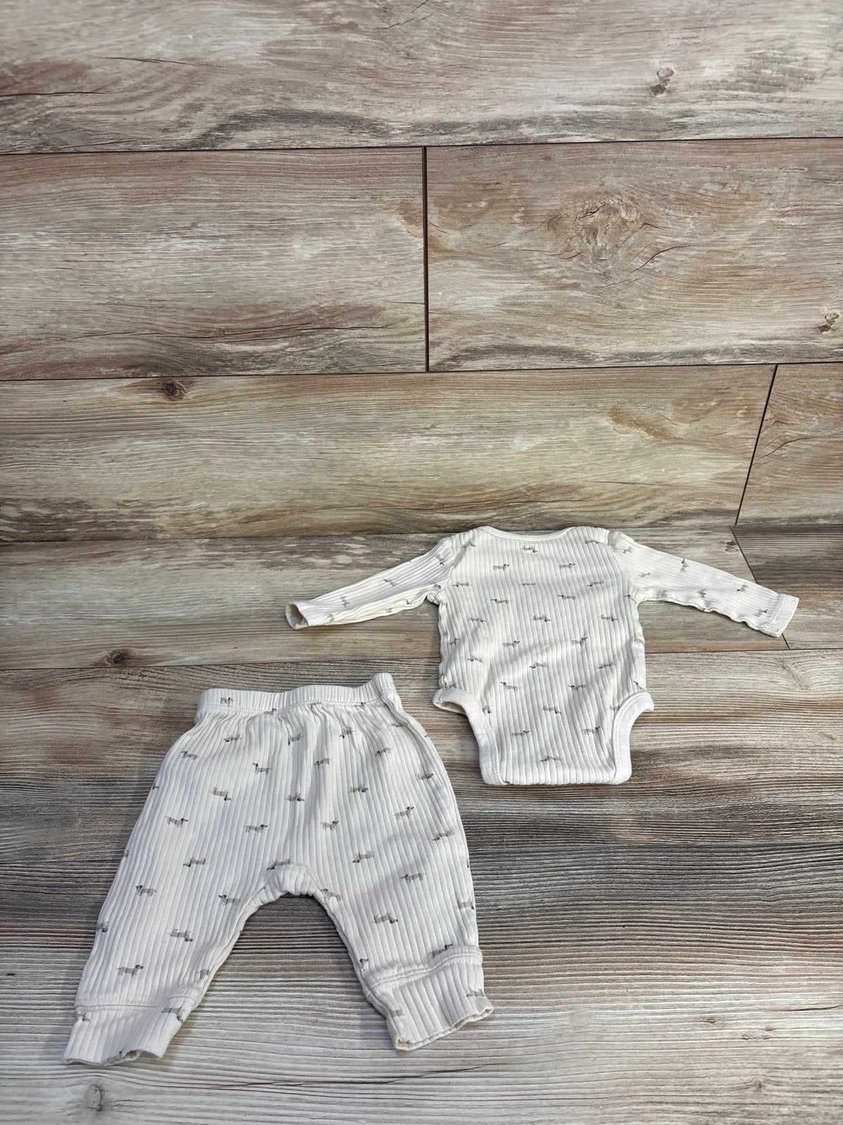 Flat lay of ivory ribbed 2-piece newborn bodysuit and pants showing ribbed texture and small gray print on wood background