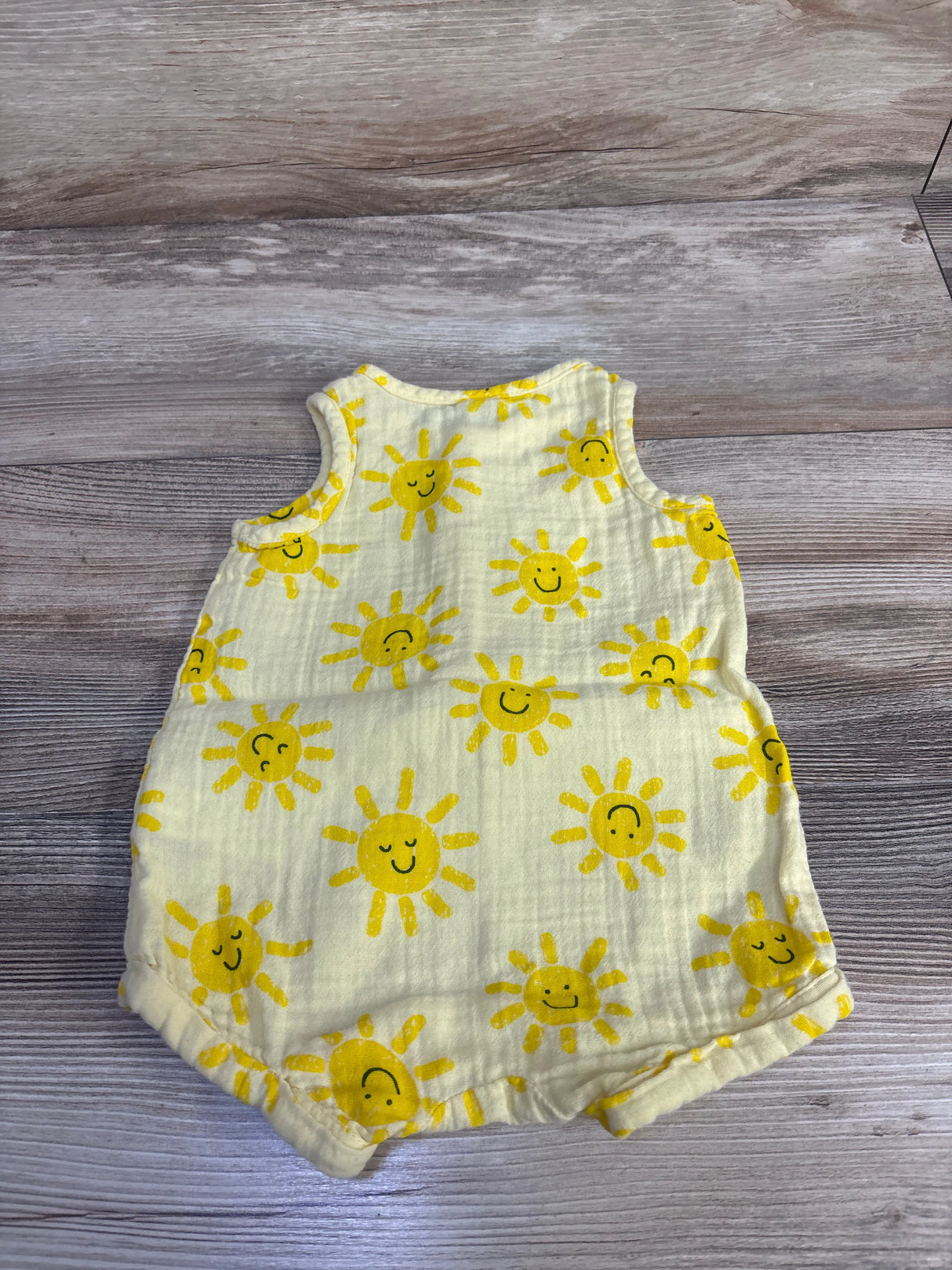 Flat lay of Old Navy sleeveless henley baby romper in sunshine yellow showing smiling sun print on wood background