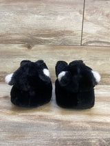 Black fuzzy baby booties with white ear accents on a wood background