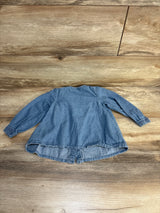 Blue denim kids long sleeve top with ruffled hem, laid flat on wood floor