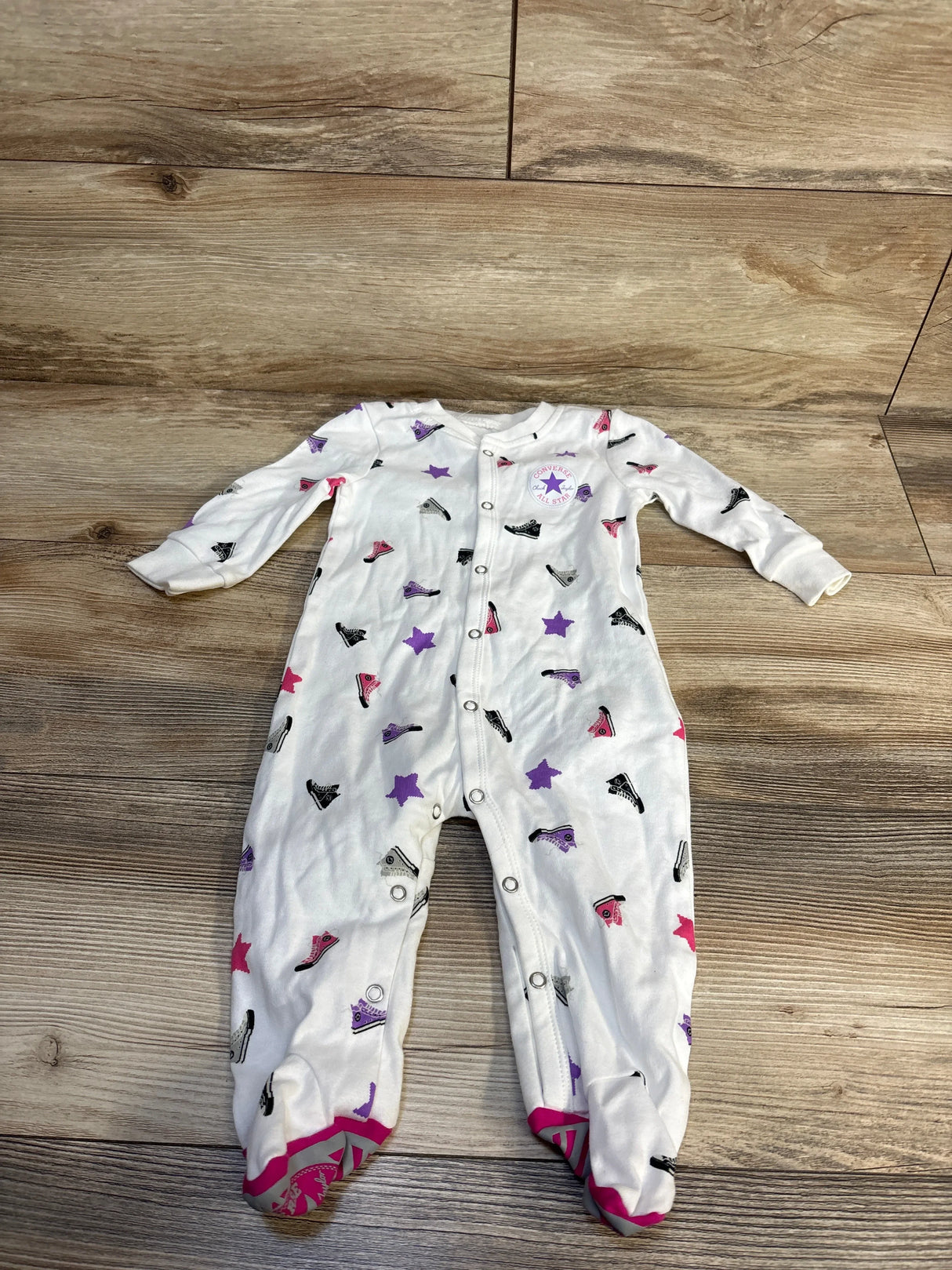 White baby onesie with Converse sneaker and star print, footed design, laid on wood floor