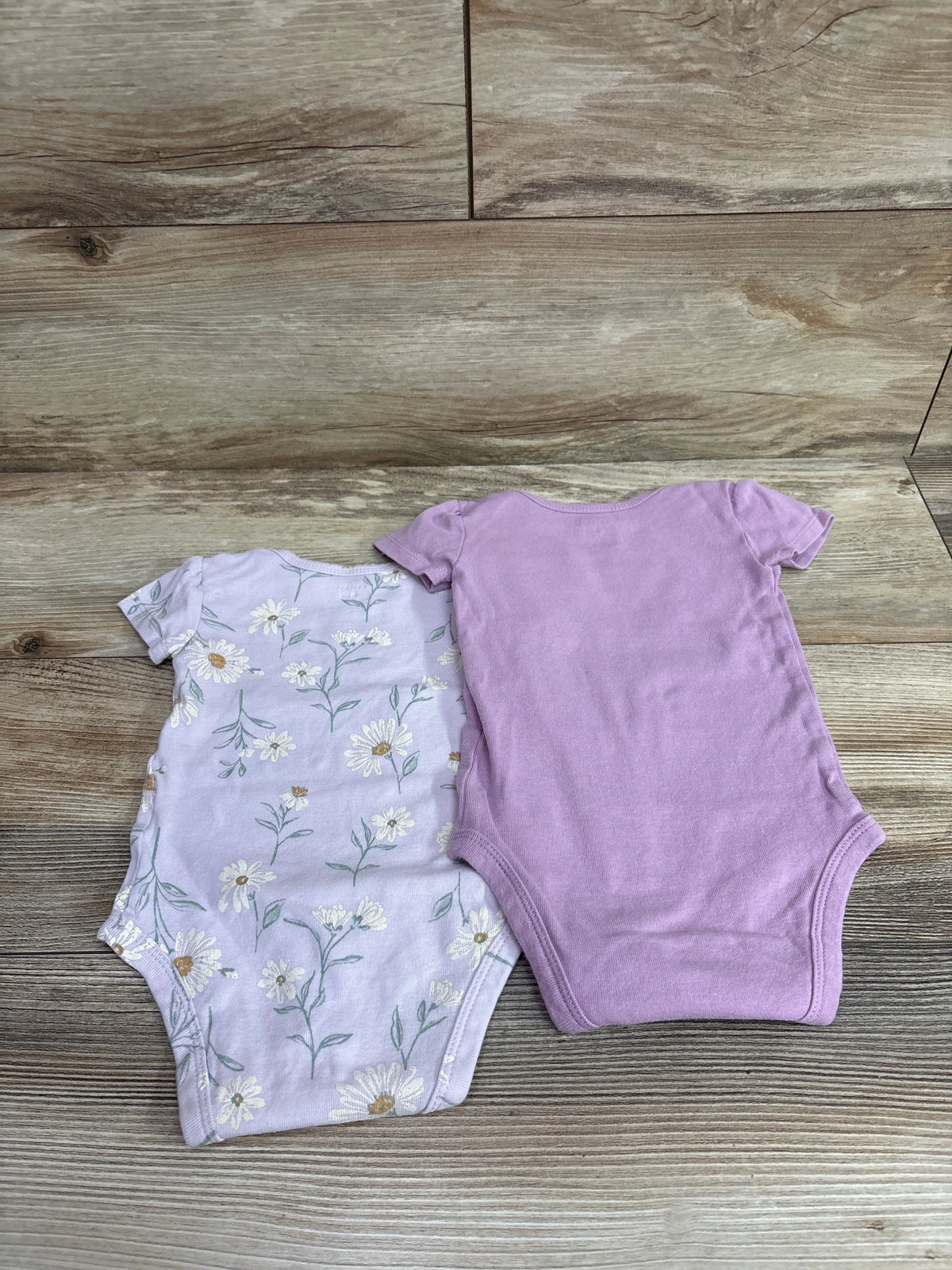 Two Carter's baby bodysuits in purple, one solid and one with a white floral print.