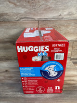 Front view of Huggies Little Snugglers newborn diaper box with 2-in-1 skincare protection, stretchy-fit diagram, on wood floor