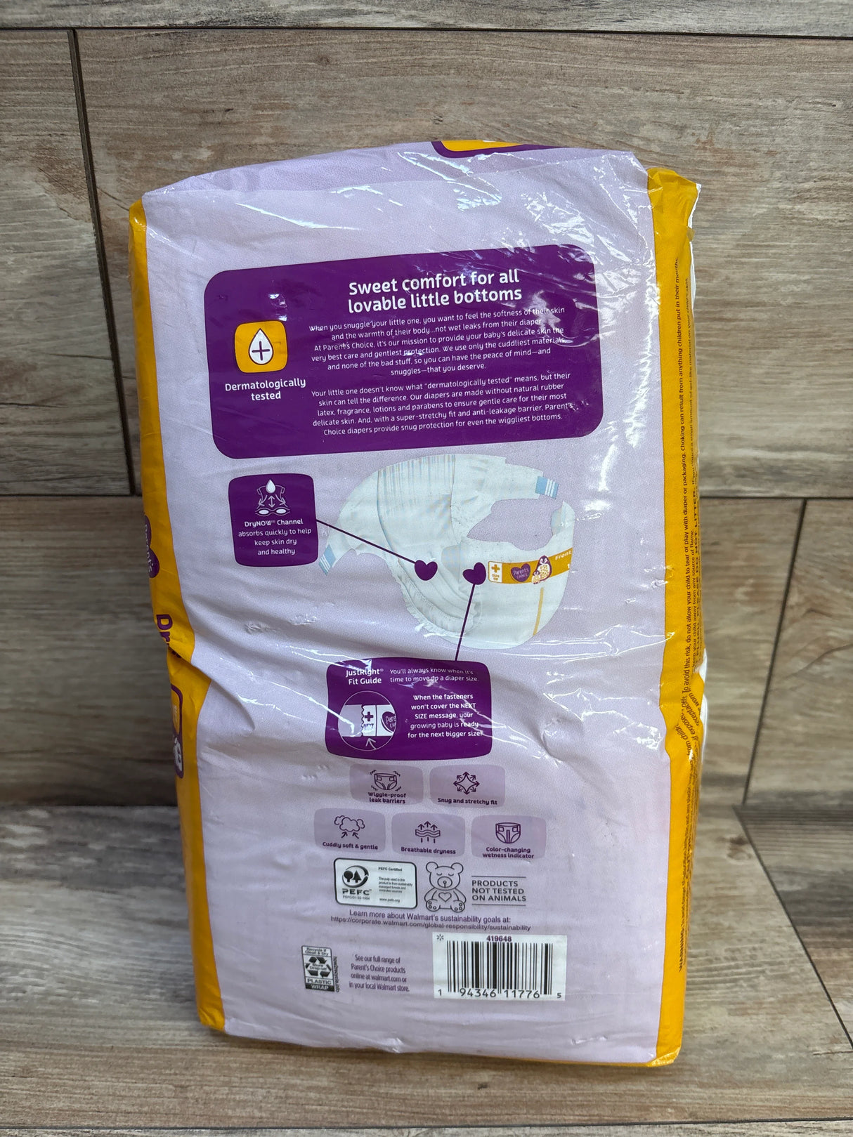 Rear view of Parent's Choice Size 1 diaper pack showcasing the purple headline Sweet comfort for all lovable little bottoms and a diaper illustration on a wooden floor background