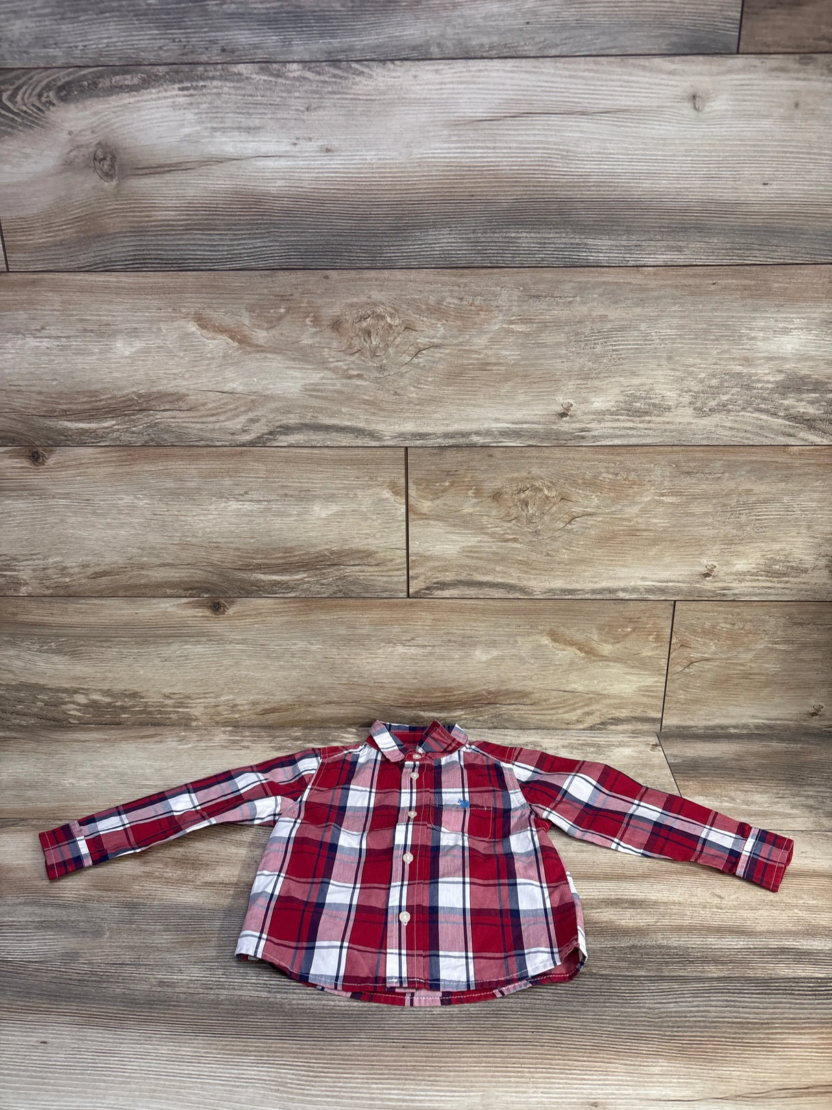 Front view of U.S. Polo Assn. toddler button-up shirt laid flat showing red plaid and chest pocket on wood background