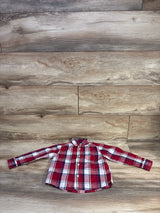 Front view of U.S. Polo Assn. toddler button-up shirt laid flat showing red plaid and chest pocket on wood background