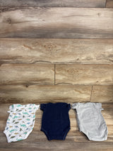 Flat lay of 3-pack 3-6M bodysuits showing dinosaur print, navy and gray solids with snap closures on wood