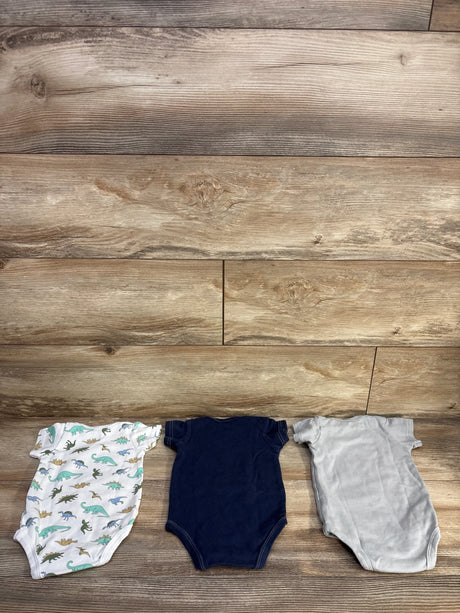 Flat lay of 3-pack 3-6M bodysuits showing dinosaur print, navy and gray solids with snap closures on wood