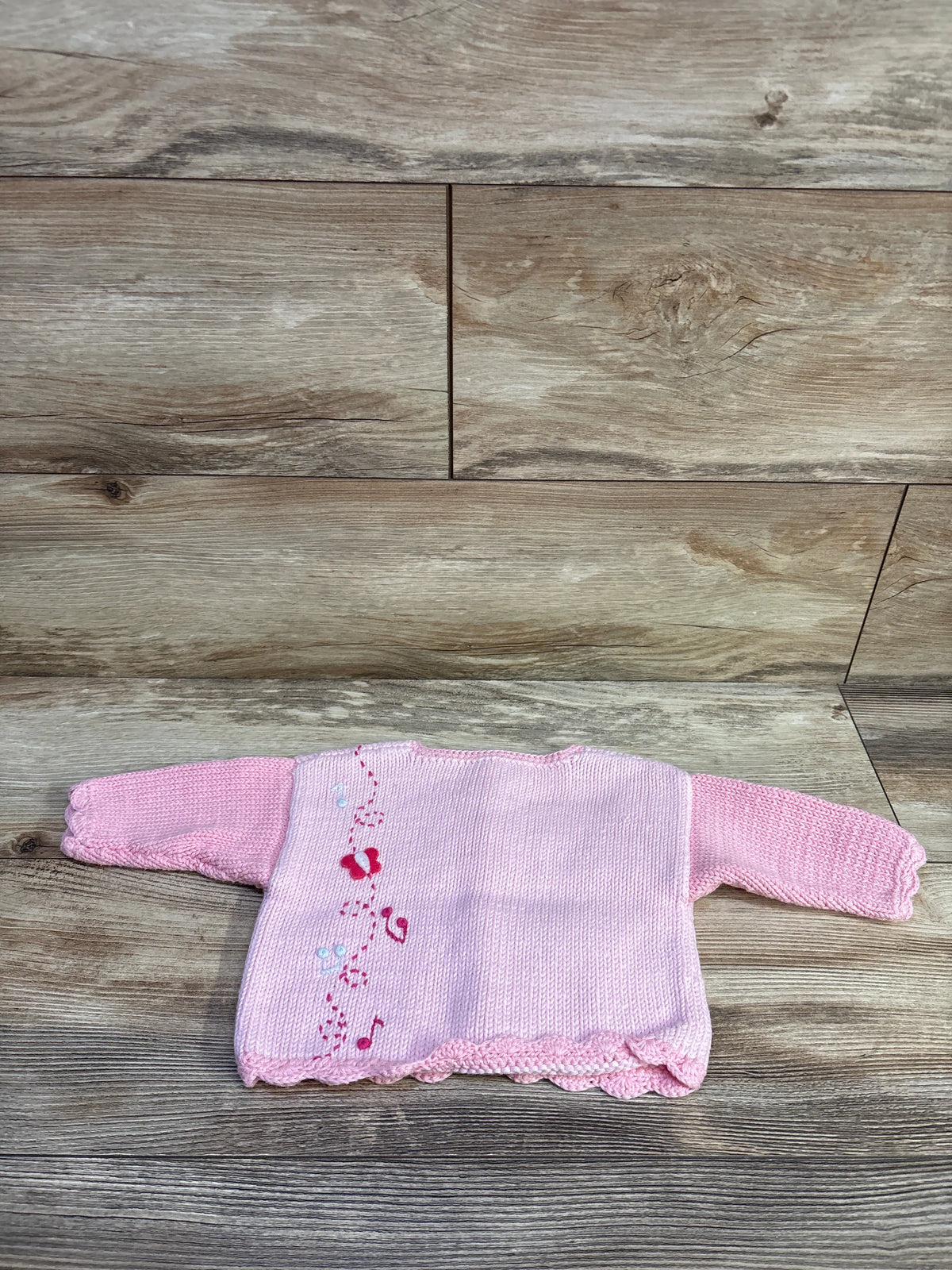 Flat lay of ArtWalk pink knit button-up cardigan for size 6 months, showcasing ballerina motifs on wood-look flooring